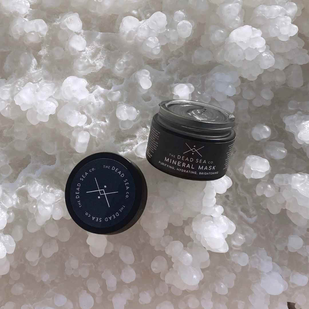 The Dead Sea Co. Dead Sea Mineral Mud Mask with lid off sitting on Dead Sea salt at the Dead Sea