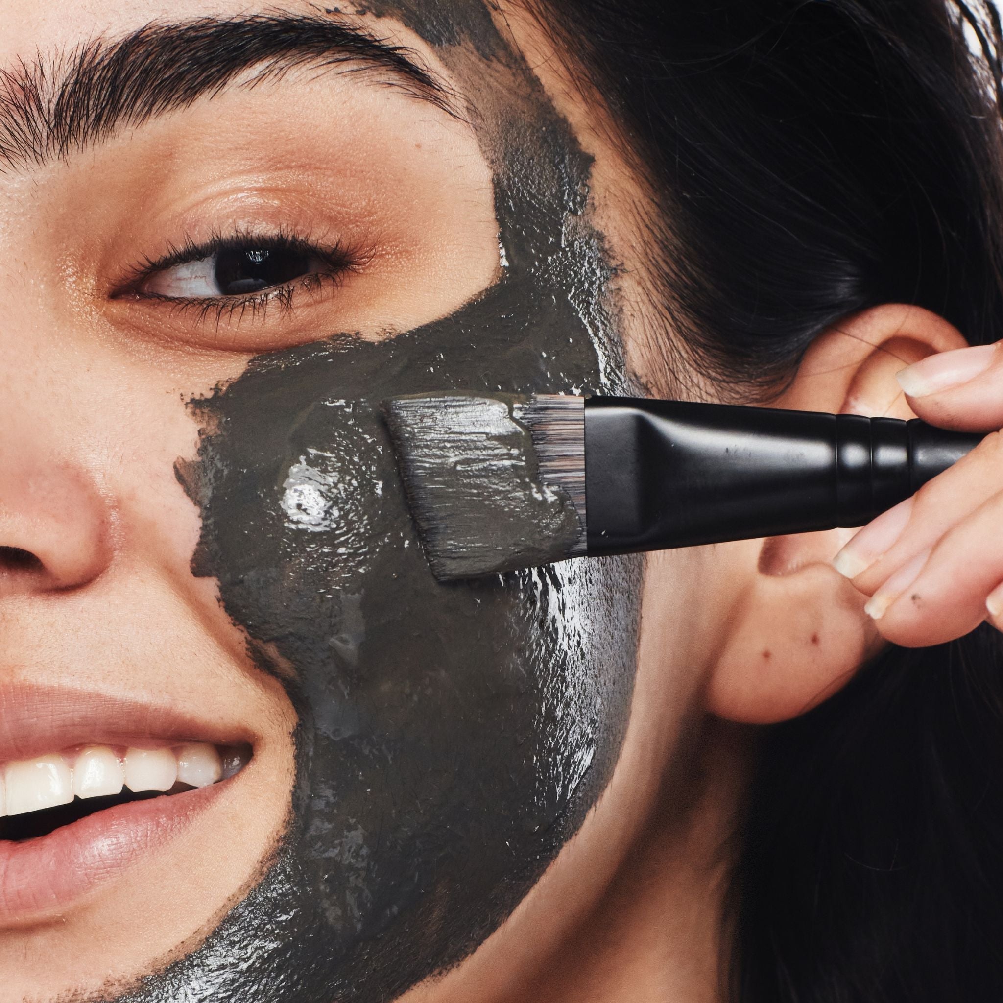 close up of face with mud mask, applying mud mask using a brush