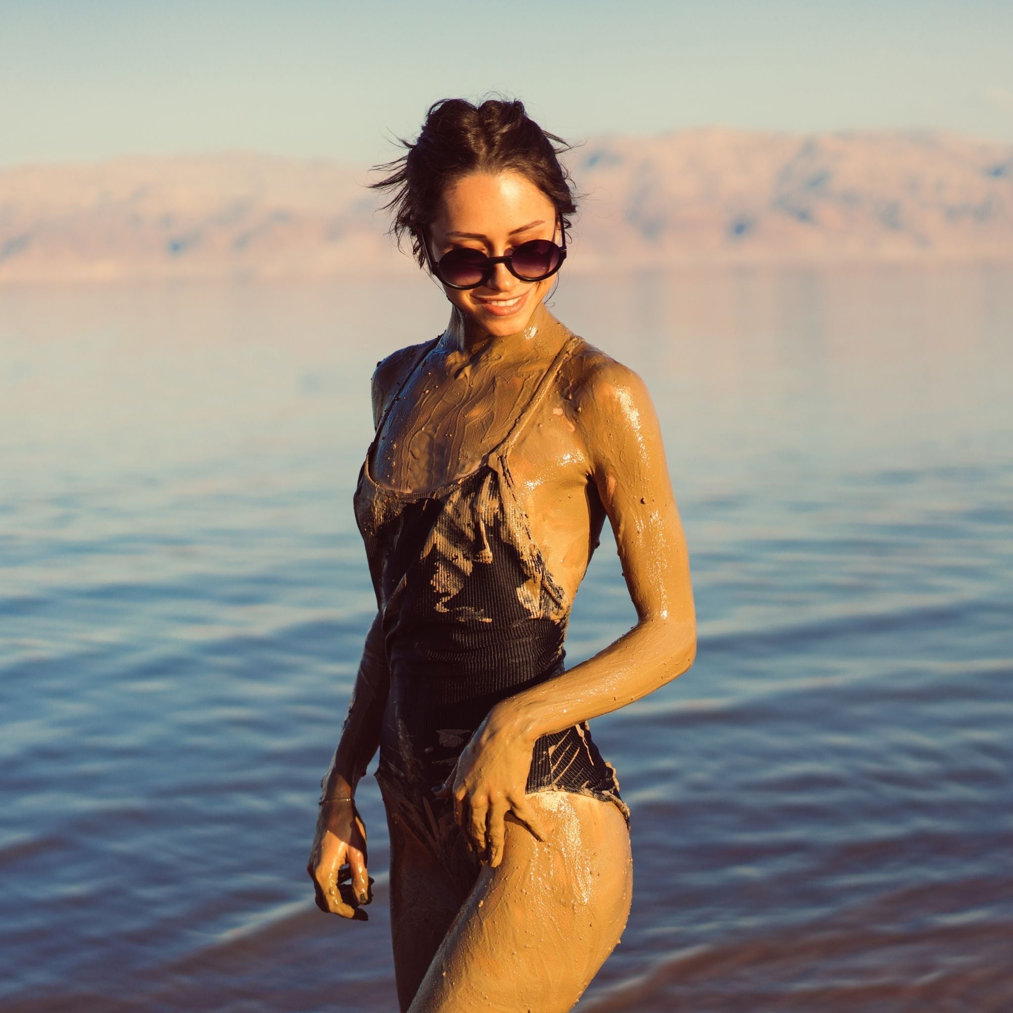 lady in swimsuit covered in mud mask, girl standing, deadsea behind