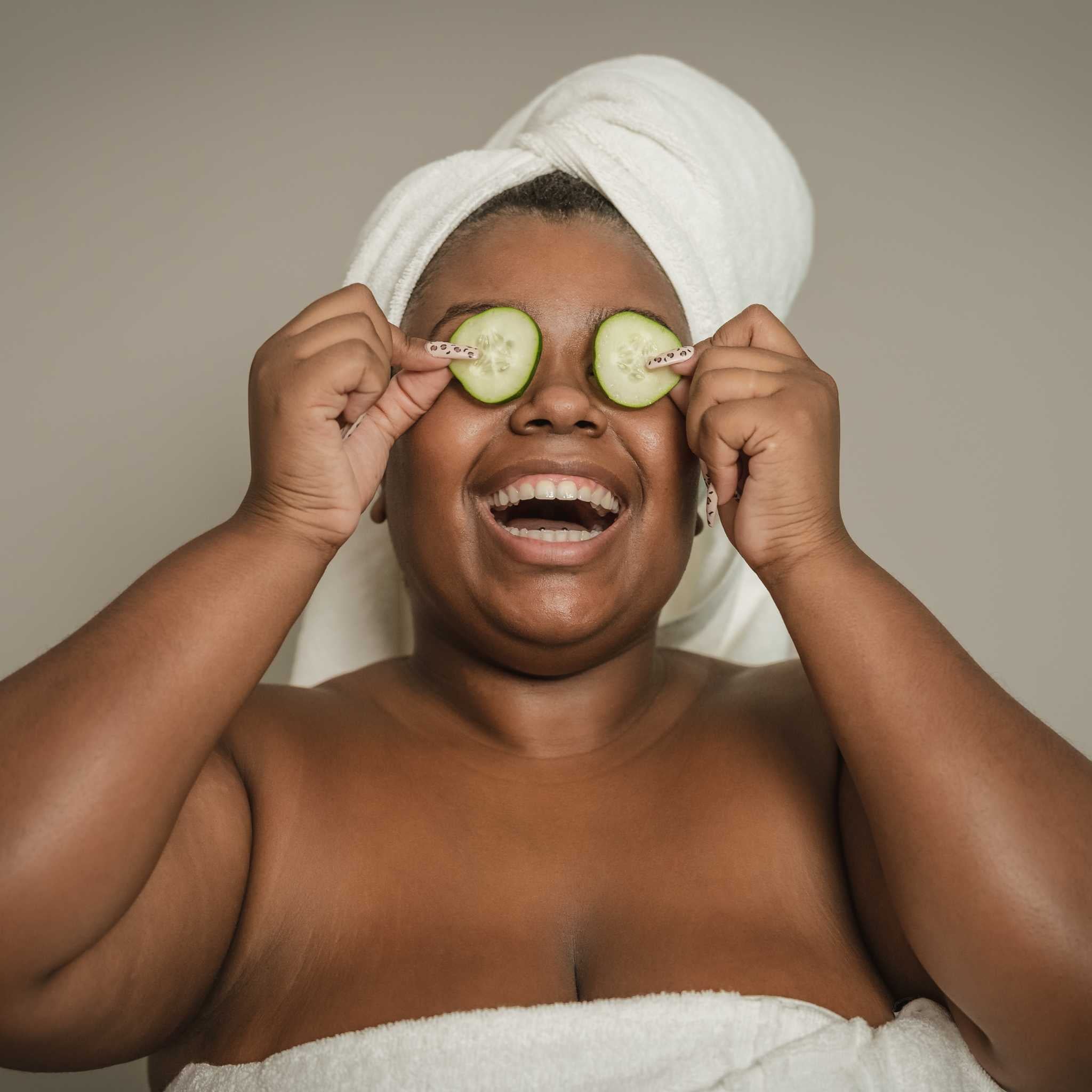 Woman practising self-care by putting cucumber slices on her eyes.