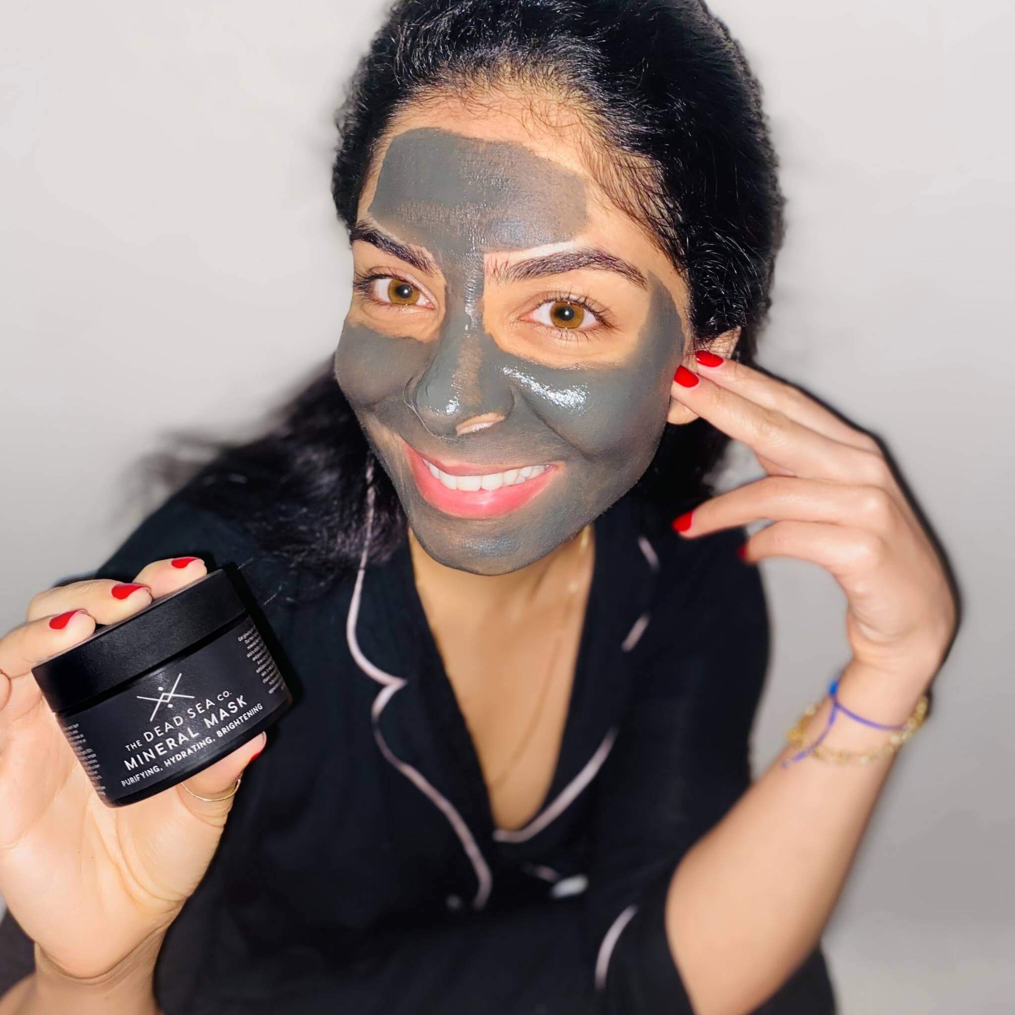 Woman using Dead Sea mud mask and holding the luxurious packaging
