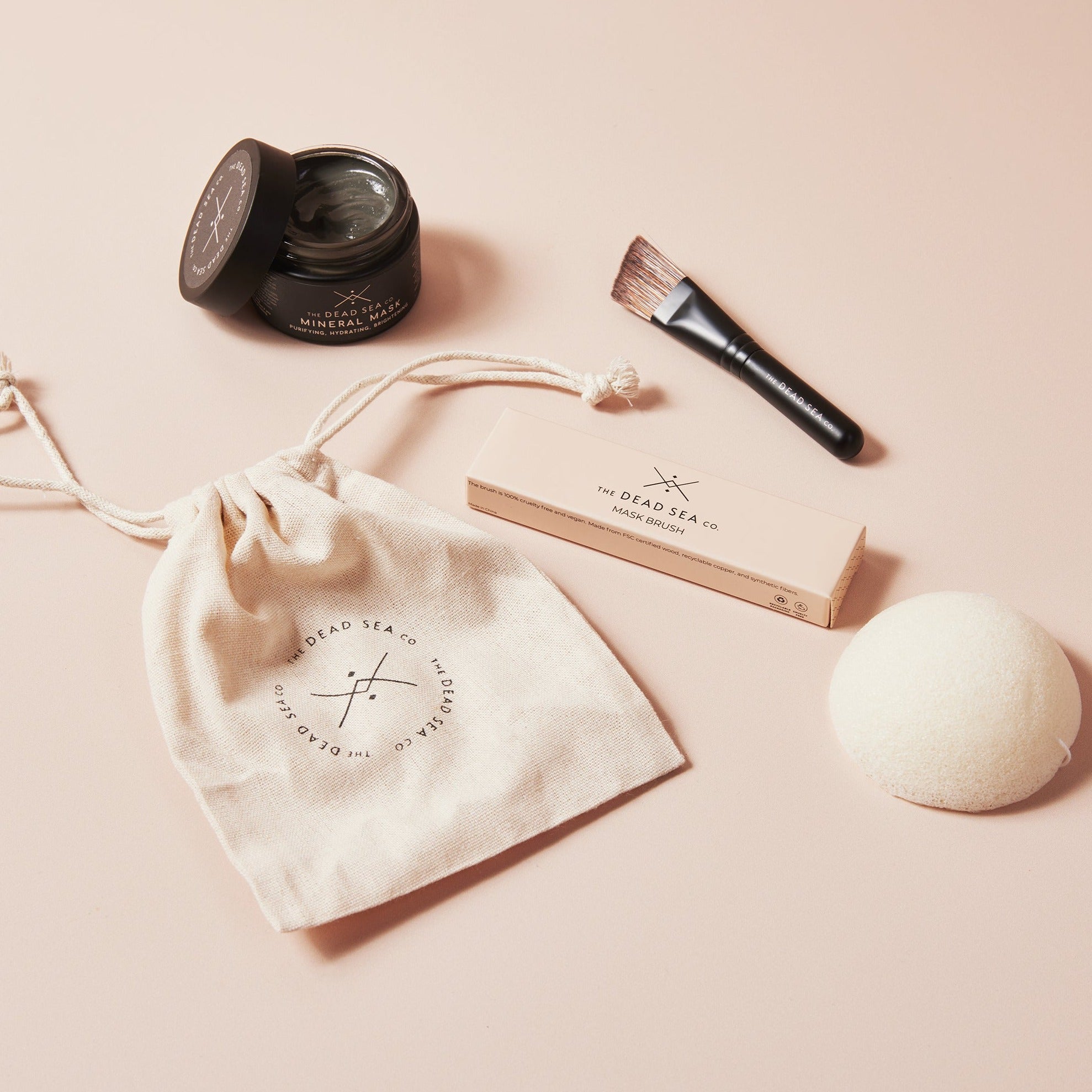 Dead Sea Mineral Mask with open lid showing creamy texture with angled face mask brush, konjac sponge and The Dead Sea Co. branded linen bag