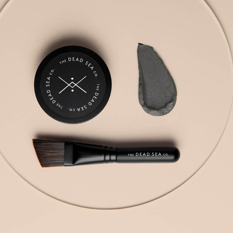 Purifying mud mask and accompanying face mask brush for an at-home spa experience, featuring a visible mud smear to showcase the product's texture.