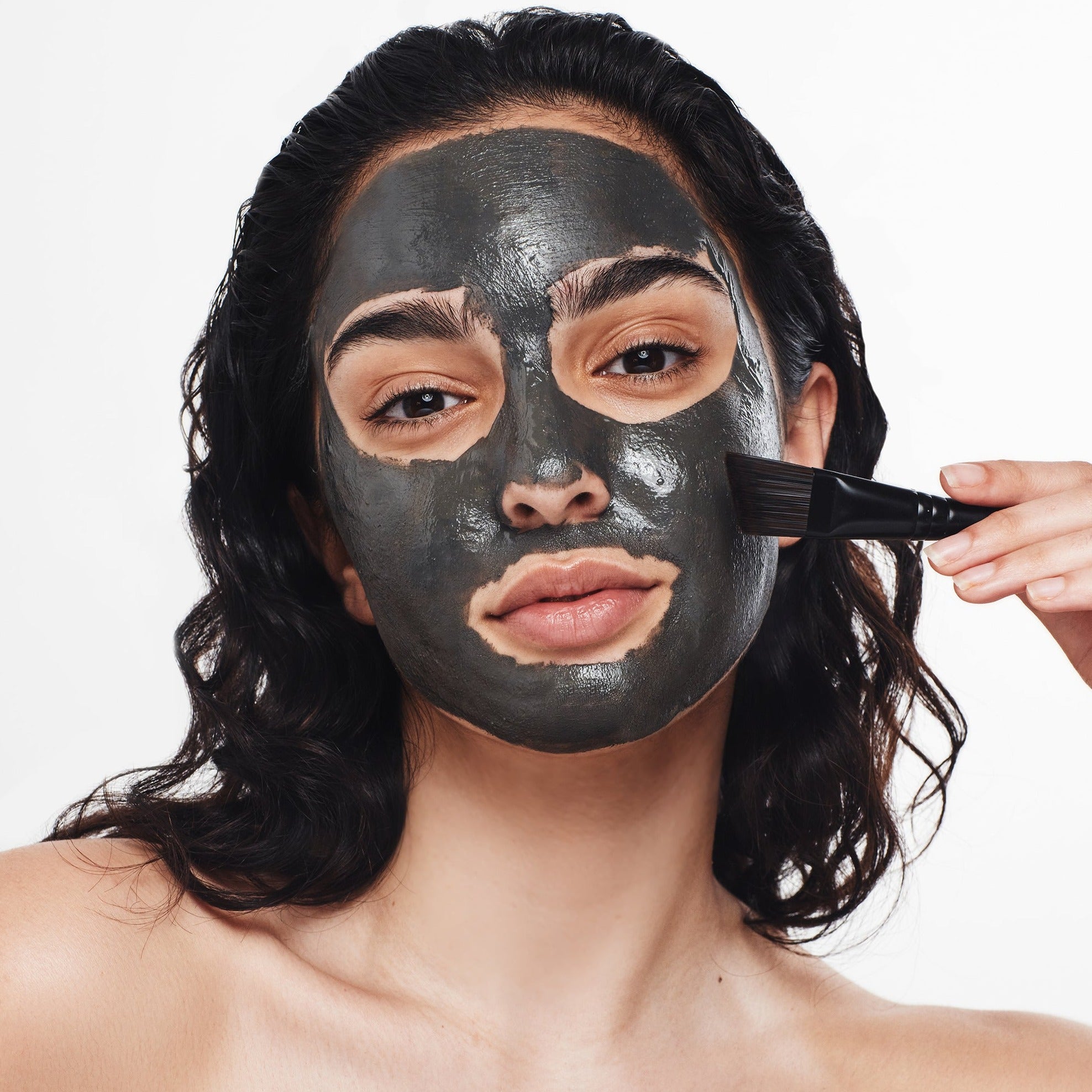 Skincare routine: Woman applying a Dead Sea mud mask using The Dead Sea Co.'s angled brush for precise application.