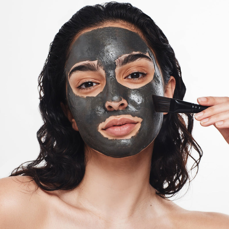 Skincare routine: Woman applying a Dead Sea mud mask using The Dead Sea Co.'s angled brush for precise application.